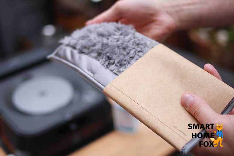 Das Trockenwischtuch des iRobot Braava jet m6 wird in den Händen gehalten, wobei der Wischroboter selbst im Hintergrund zu sehen ist